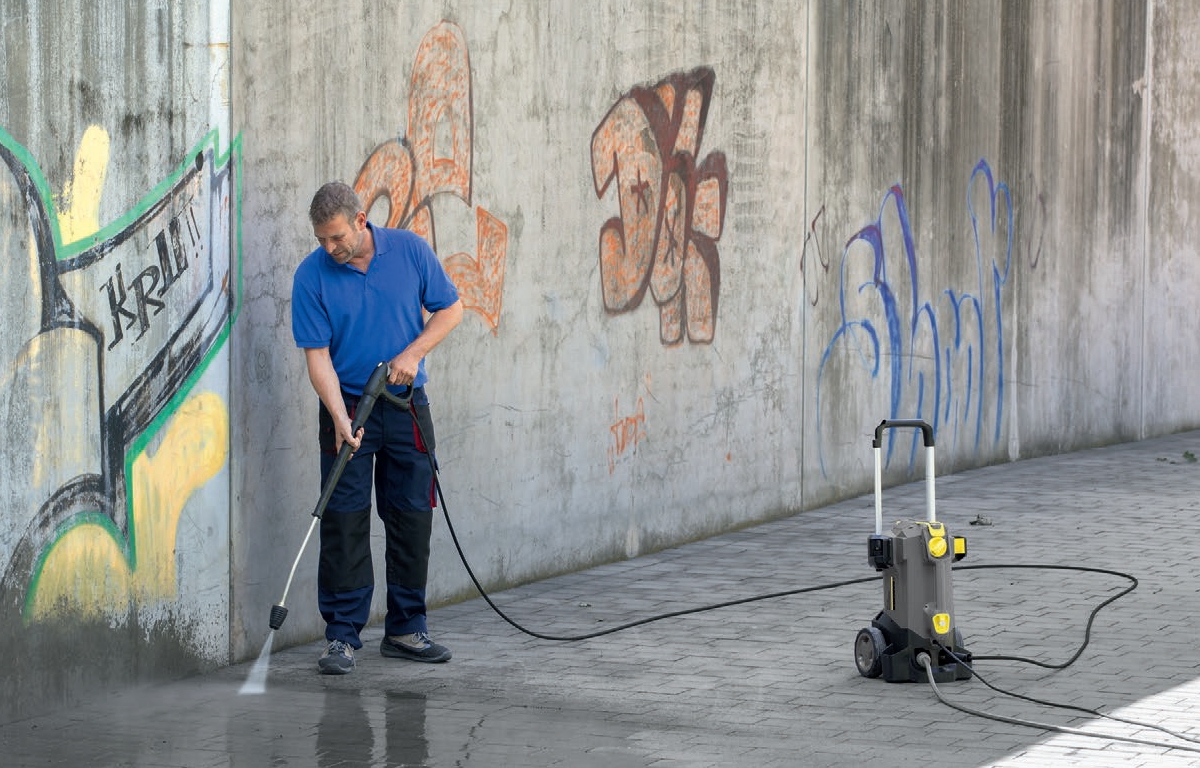 Profesjonalna myjka wysokociśnieniowa HD 5/12 C firmy Karcher podczas mycia chodnika i ścian z graffiti.